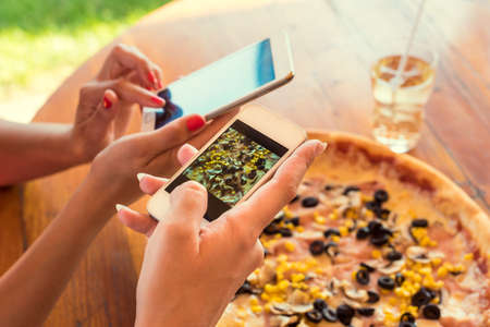 Female friends using smartphones to take photos of their pizzaの写真素材