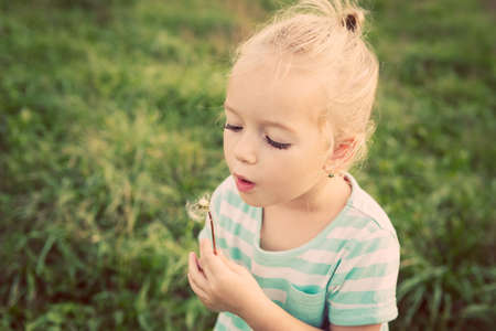 Adorable little blond girl with dandelion flower. Happy kid having fun outdoorsの写真素材
