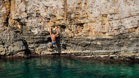 Young athletic man climbing sea cliffs without rope or harness in Croatia