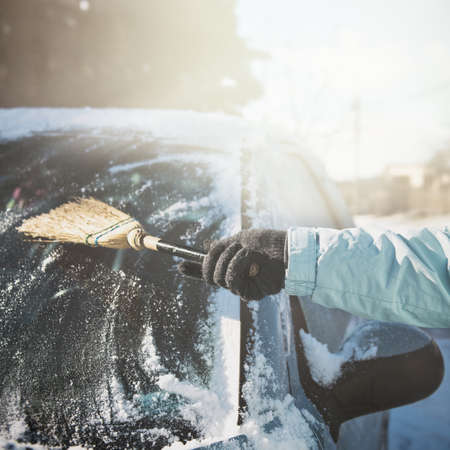 Transportation, winter, weather, people and vehicle concept - woman cleaning snow from her car with a broomの写真素材