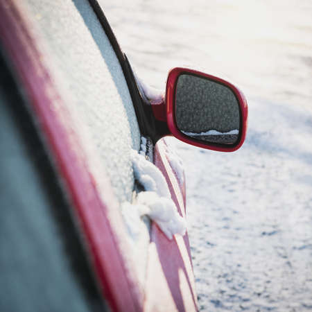 Frozen red car parked outside, with focus on rear view mirror, winter transport issues