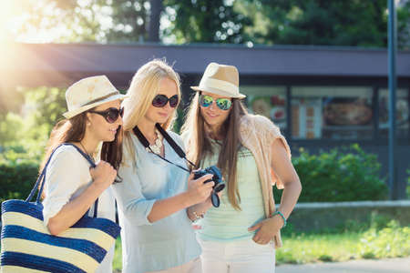 Three attractive girls looking at photos on their camera at summer holidays, girl friends on their travel vacationの写真素材