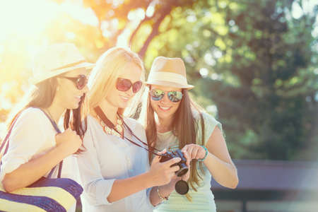 Three attractive girls looking at photos on their camera at summer holidays, girl friends on their travel vacationの写真素材