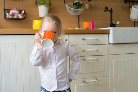 Cute blond girl holding a large cup of tea in the kitchenの写真素材