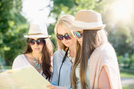 Friends looking for directions on a map at summer holidays, vacation concept