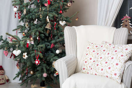 Beautiful holiday decorated room with Christmas tree and white comfortable chair with soft blanket and cushionの写真素材