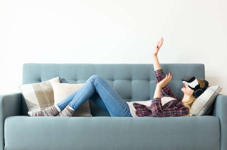 Attractive woman wearing virtual reality goggles lying on a couch. Virtual reality headset....