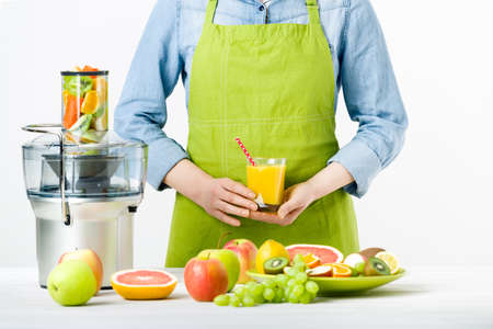 Anonymous woman wearing an apron, holding glass of freshly pressed juice, healthy lifestyle concept on white backgroundの写真素材