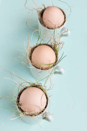 Uncolored natural easter eggs in espresso cups; happy easter concept; green minimalist easter backgroundの写真素材