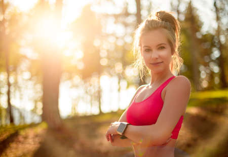 Attractive fit athletic woman in a forest, wearing smart watch, taking a break from intense workout. Sport, fitness, workout conceptの写真素材