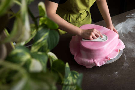 Unrecognisable woman in bakery decorating heart shaped wedding cake with pink fondant, view from aboveの写真素材