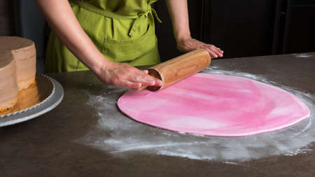 Woman using rolling pin preparing pink fondant for cake decorating, hands detailの写真素材