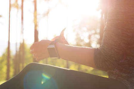 Lifestyle wearable technology shot with lensflare. Female athlete putting on her her smart watch to monitor workout performanceの写真素材
