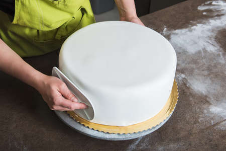 Unrecognisable woman in bakery decorating wedding cake with white fondantの写真素材