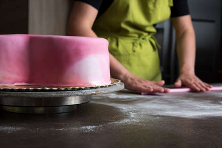 Unrecognisable woman preparing pink fondant for cake decorating, focus on the cakeの写真素材