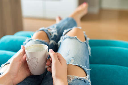 Beautiful young woman relaxing on the sofa at home, watching tv and enjoying coffeeの写真素材