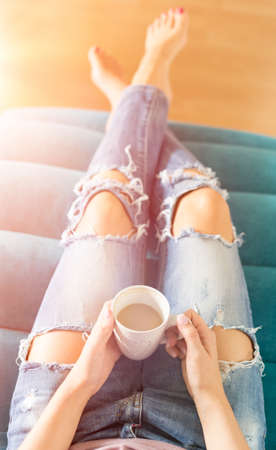 Beautiful young woman relaxing on the sofa at home, watching tv and enjoying coffee