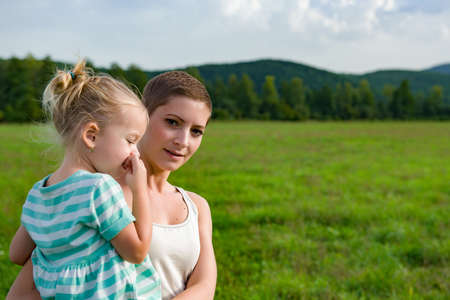 Attractive young mother carrying preschool daughter in her arms during a walk through a meadowの写真素材