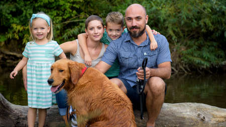 Beautiful young family with their pet dog, golden retriever, on a trip by a riverの写真素材