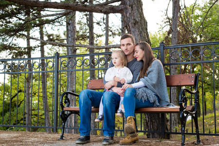 Happy family of three sitting on a bench in a park enjoying their time together.の写真素材