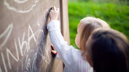 Cute little girl drawing on blackboard. Toddler girl having fun outdoors, holding chalk and drawing.の写真素材