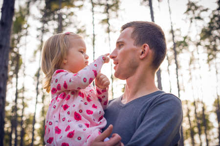 Young father holding cute toddler girl daughter in his arms and looking at herの写真素材