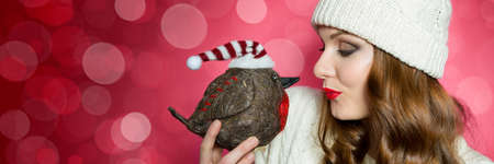 Gorgeous woman in knitted jumper and a hat sending a kiss to robin the christmas bird. Funny xmas...
