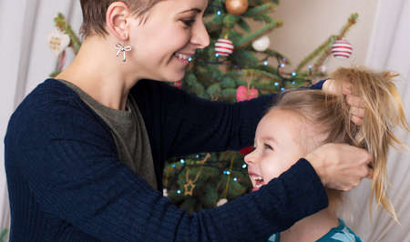 Authentic family christmas portrait in front of xmas tree. Smiling mother and daughter enjoying christmasの写真素材