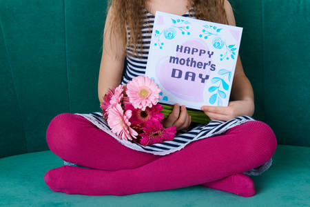 Unrecognisable young girl sitting on a couch, holding bouquet of pink gerbera daisies and Mother's...