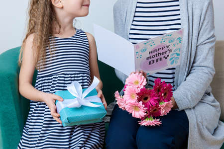 Happy Mother's Day. Cute little girl giving mom greeting card, present and bouquet of pink gerbera daisies. Mother and daughter concept.の写真素材