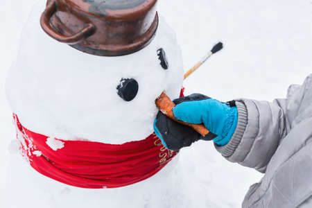Authentic family winter fun. Young child building a snowman. Candid real people lifestyle image of making a snowman. Boy holding snowman by its carrot nose.の写真素材