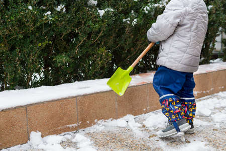 Child helping clearing snow from sidewalk. Candid authentic family winter activities. Snow shoveling concept.の写真素材