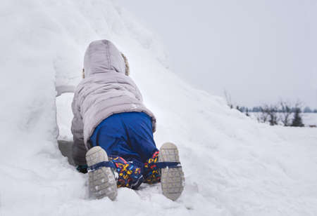 Young child crawling into a snow fort build in a backyard. Hide and seek. Winter family fun activities.の写真素材