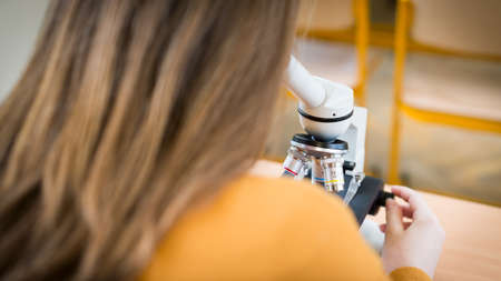 High School female student in biology class. Student using microscope to examine samples.の写真素材