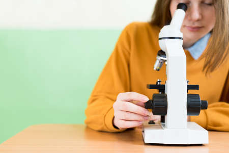 High School female student in biology class. Student using microscope to examine samples.の写真素材