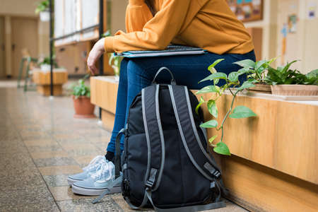 Young unrecognisable depressed lonely female college student sitting in the hallway at her school. Education, Bullying, Depression concept.の写真素材