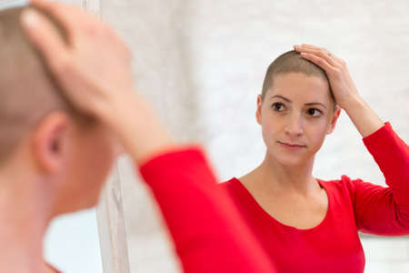 Young adult female cancer patient looking in the mirror, stroking her new short hair. の写真素材