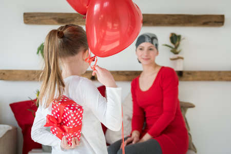 Young mother, cancer patient, and her cute daughter, celebrating return home from hospital. Welcome home or birthday party with balloons and presents.の写真素材