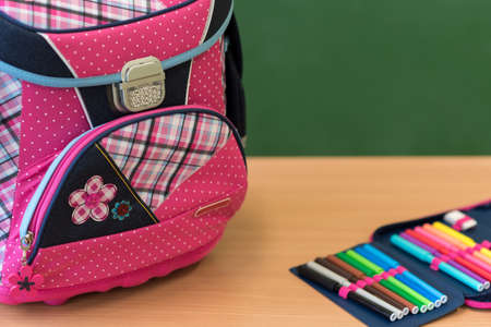 Pink girly school bag and pencil case on a desk against greenboard. First day of school concept.