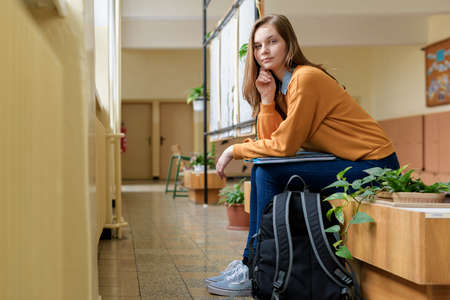 Young happy female college student sitting in the hallway at her school. Education concept.の写真素材