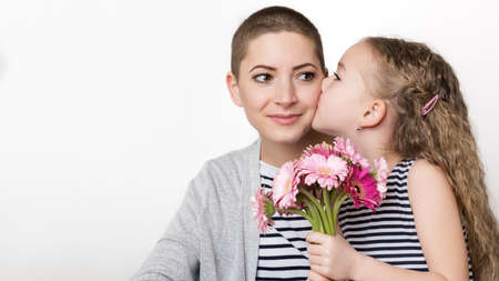 Happy Mother's Day, Women's day or Birthday background. Cute little girl giving mom, cancer survivor,  bouquet of pink gerbera daisies. Loving mother and daughter.の写真素材