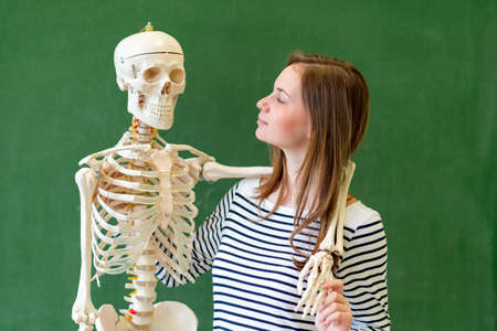 Cool female high school student portrait with an artificial human body skeleton. Student having fun...