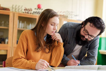 Young male hispanic teacher helping his student in chemistry class. Education, Tutoring and...