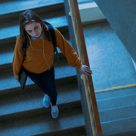 Young depressed lonely female college student walking down the stairs at her school, looking down....