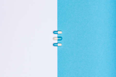 White and blue pills isolated on bicolor white and blue colored background. Medication and prescription pills minimal flat lay with copy space.の写真素材
