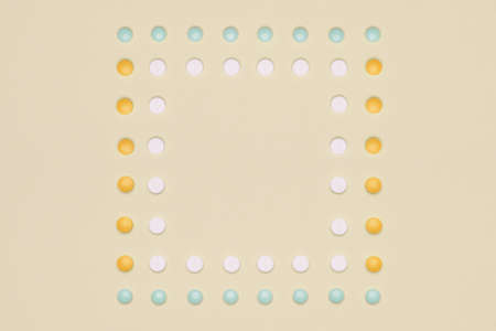 Assortment of various colourful pills in a row, isolated on yellow, pastel coloured background....