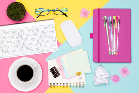 Office Desk Working Space Flat Lay. Top view photo of workspace with keyboard, notepad, coffee cup and glasses on pastel background. Pastel pink, yellow and blue color working desk concept.の写真素材
