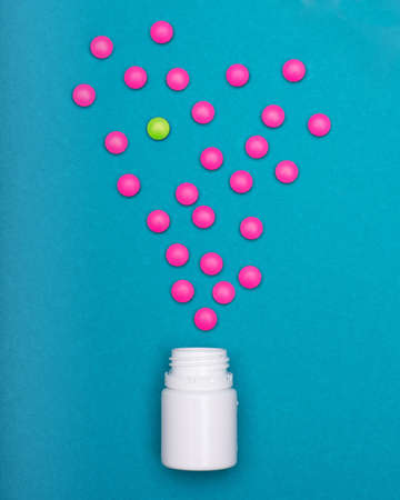 Medication bottle and bright pink pills spilled on dark blue coloured background. Medication and...