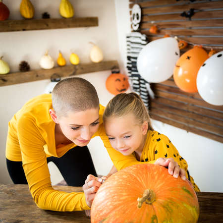 Mother and daughter drawing smiley anthropomorphic; face on a large Halloween pumpkin. Family decorating pumpkin.の写真素材