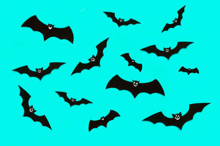 Halloween and decoration concept. Cute smiling black paper bats flying over pastel blue background....